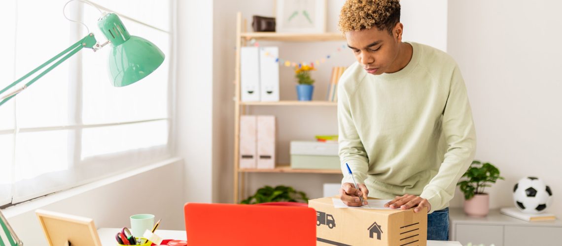 Hispanic latin young seller man preparing second hand package before sending to buyer - Young male seller writing address on box